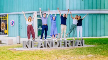People jumping on 'Neandertal' sign outdoors.