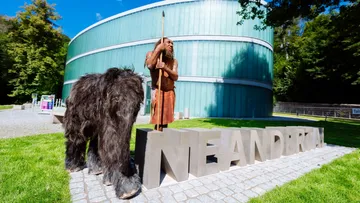 Neanderthaler-Statue und Tier vor Museum.