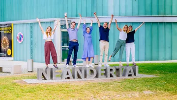 Menschen springen vor dem Neanderthal-Museum.