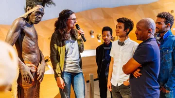 Gruppe hört einer Frau in Museum zu.