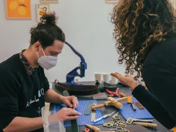 Man works on crafts, woman explains in creative space.