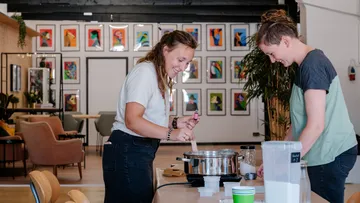 Two women cooking together in an art-filled room.