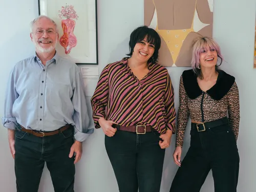 Three people smile together in front of colorful works of art.