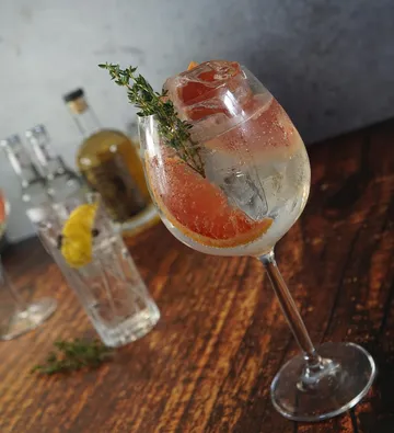 Gin Tonic mit Garnitur auf Holztisch.