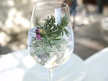 Glas mit Kräutern und Blume auf Tisch.
