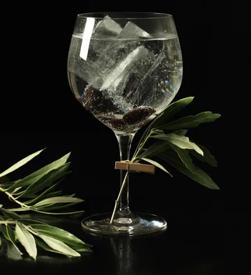 Cocktailglas mit Eis und Olive, dunkler Hintergrund.