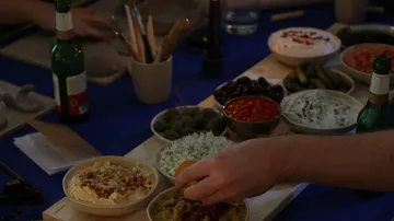 Hand greift nach Essen auf einem Esstisch.