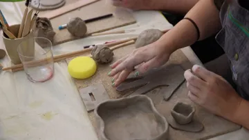 Hands shaping pottery clay on a table.