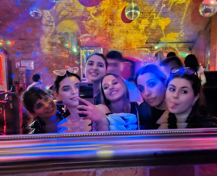 Six women taking a selfie in a colorful club.
