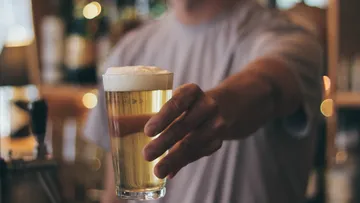 Person hält Bierglas an der Bar.