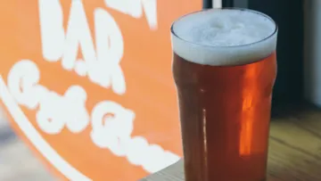 Pint of beer on wooden table, orange sign background.