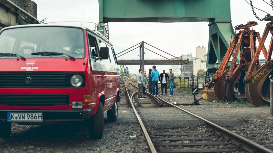 Red van parked near railway tracks, people standing nearby.