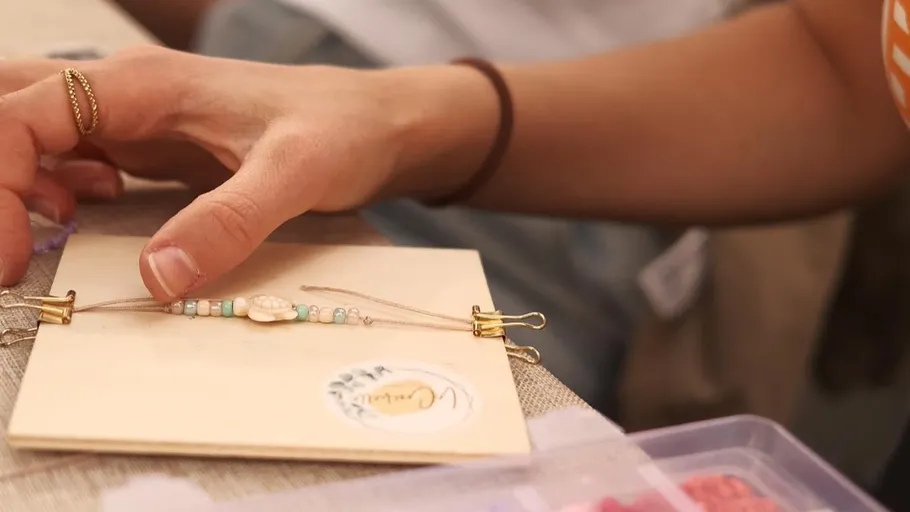 Hand fertigt Perlenarmband auf Schreibtisch.