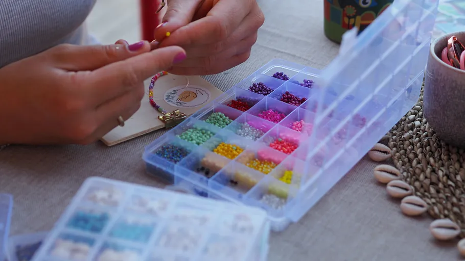 Hände fertigen Perlen-Schmuck an einem Tisch.