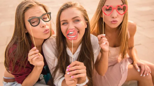 Three women holding playful mask props outdoors.