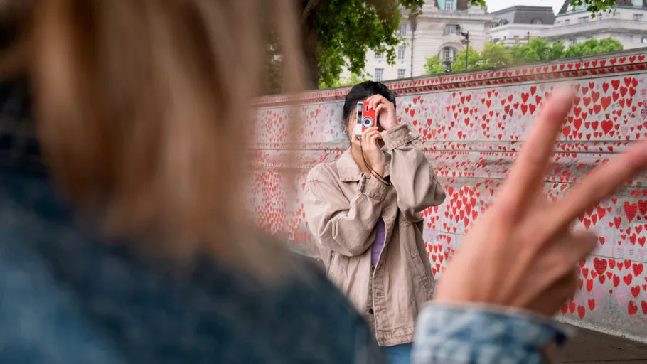 Person photographing someone near heart-covered wall.