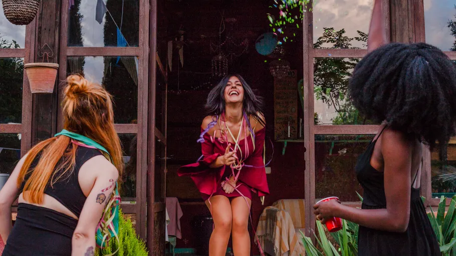 Three women celebrating outside a wooden house.