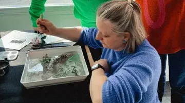 Woman painting on water, art tools nearby.