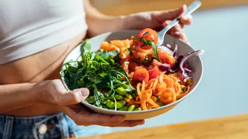 Person holding bowl of fresh vegetables.