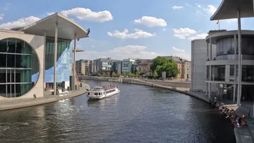 Boat sailing on river by modern buildings.