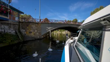 Boat near bridge with swans in canal.