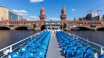 Boat with blue chairs facing historic bridge.