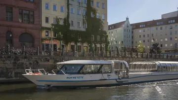 Tour boat on a river, city buildings background.