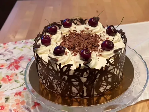 Dekorativer Kuchen mit Kirschen und Schokolade darüber.