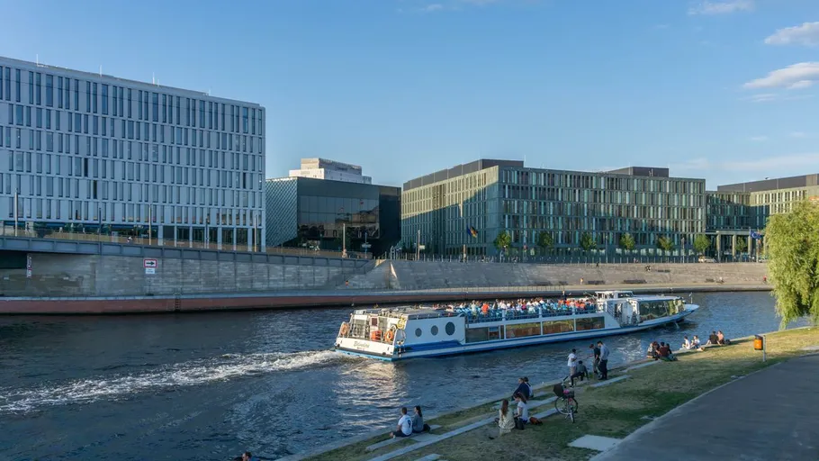 Tourboot fährt auf Fluss, moderne Gebäude dahinter.