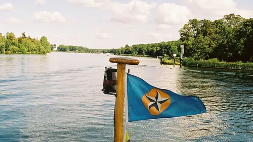 Flag on a boat, river surrounded by trees.
