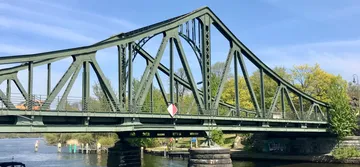 Grüne Metallbrücke über ruhigen Fluss.