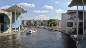 Boat cruising past modern riverside buildings.