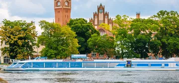 Boot fährt auf Fluss, historisches Gebäude im Hintergrund.