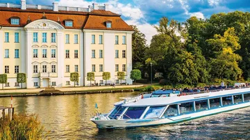Boat cruising past elegant riverside mansion.