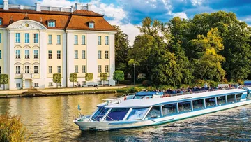Boat cruising near elegant riverside mansion.