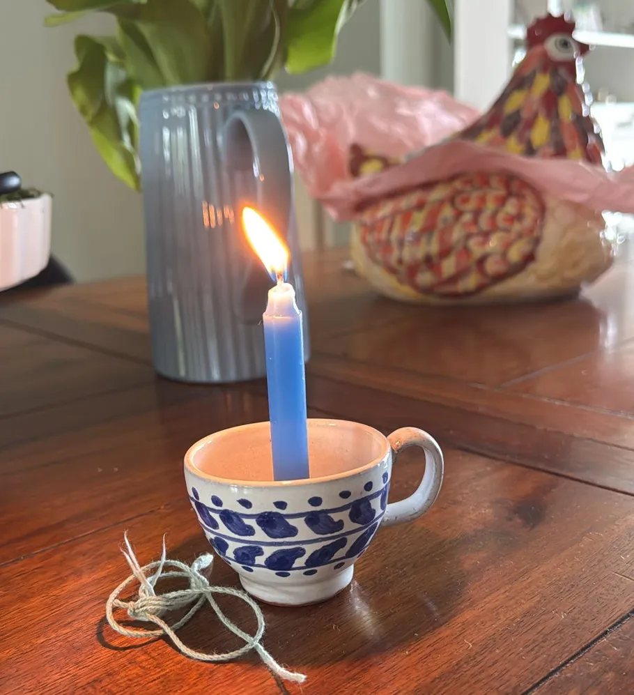 Blue candle lit in decorative cup on table.