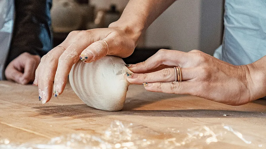 Hands shaping dough on a wooden table.