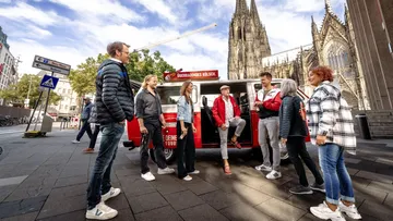 People talking near a red van, cathedral background.