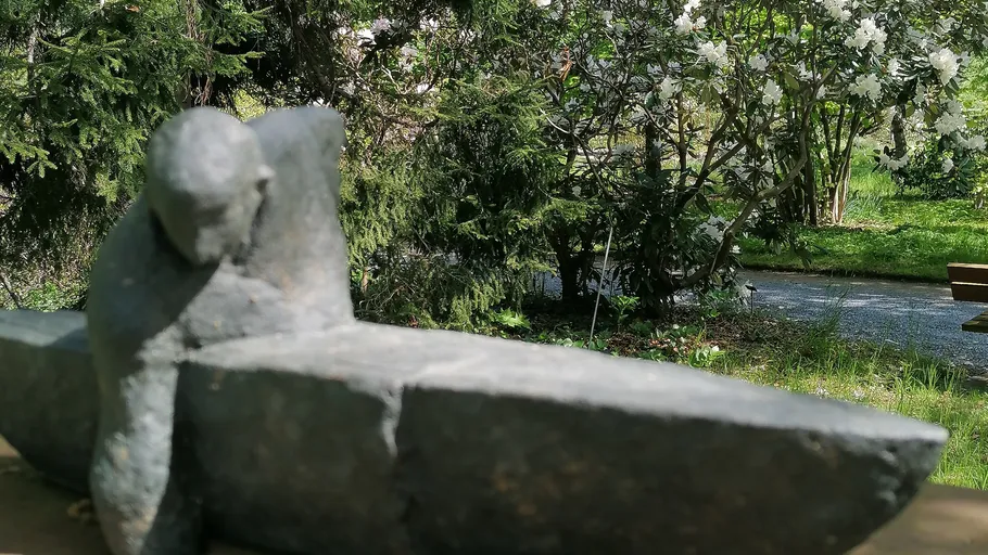 Stone sculpture leaning on ledge, garden background.