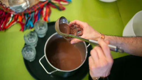 Person pouring hot chocolate into a glass.