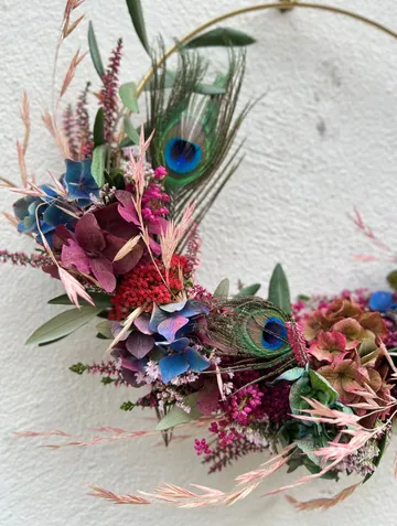 Floral wreath with peacock feathers on wall.