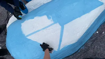 Hands spray painting blue rock surface.