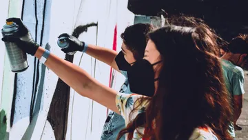 Menschen sprühen gemeinsam eine Wand an draußen.