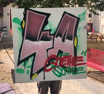 Person holding graffiti board, outdoor setting.