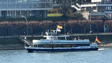 Boot fährt auf Fluss nahe der Uferpromenade.