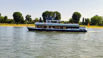 Fähre fährt auf Fluss, umgeben von Bäumen.