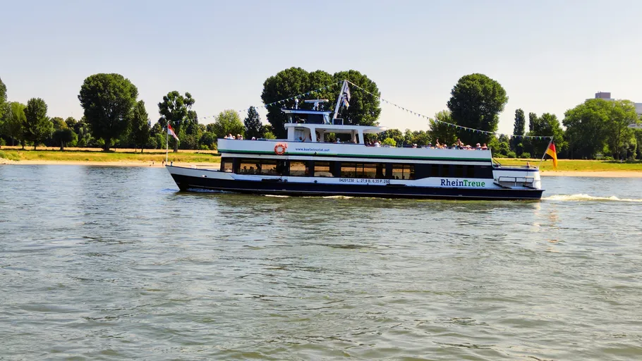 Ferry sailing on river, lined with trees.