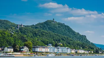 Buildings by river with forested hill background.