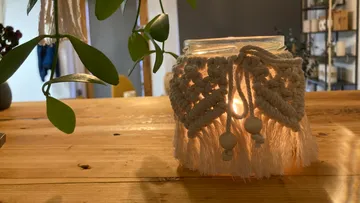 Macramé-covered jar candle on wooden table.