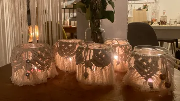 Candles in jars with macramé on a table.
